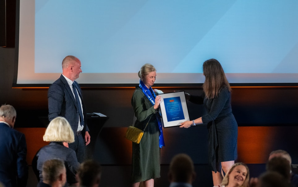 Birgitte Davidsen, faglig leder i Olaf B. Terjesen, står på scenen for å ta i mot prisen for Årets Lærebedrift 2024. Her sammen med dommer Håvard Hamansen Wallstad, daglig leder i fjorårets vinnerbedrift, Nilsson Haras AS, og Nina Solli, adm. dir. i NHO Byggenæringen. Foto: Stian Norum Herlofsen